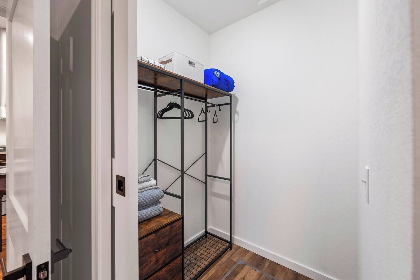 A walk-in closet with a metal shelving unit, a wooden floor, and a white wall.