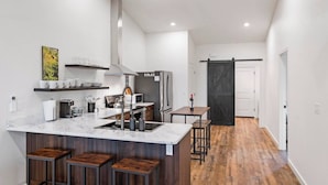 A modern kitchen with a marble countertop, wooden stools, a black sliding door, and a stainless steel refrigerator. - Bear-Themed New Duplex in Polson MT – 2BR Near Flathead Lake & Glacier (Polson)