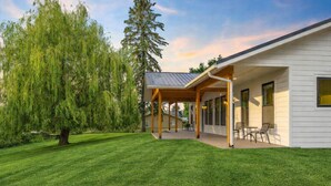 A modern house with a covered patio, a well-maintained lawn, and a large tree. - Bear-Themed New Duplex in Polson MT – 2BR Near Flathead Lake & Glacier (Polson)