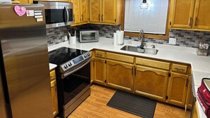 A kitchen with wooden cabinets, stainless steel appliances, a toaster, and a window with blinds.
