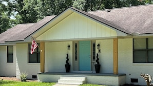 A single-story house with a front porch, a blue door, and a small garden area.