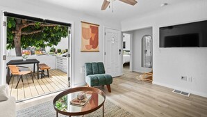 A modern living room with a wooden floor, a green armchair, a glass coffee table, and a ceiling fan. - Chic 3BR Spanish Bungalow in Walkable North Park (San Diego)