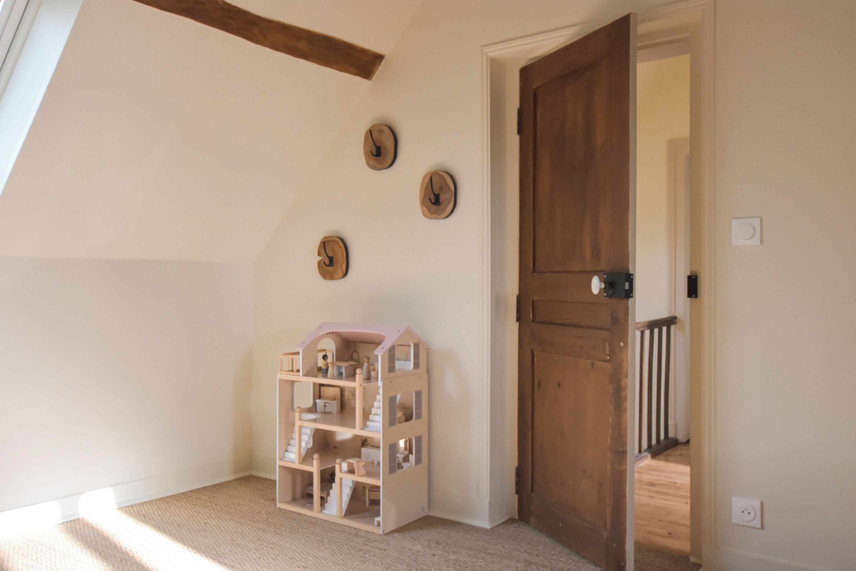 Una habitación con una puerta de madera, una casa de muñecas y tres relojes de pared.