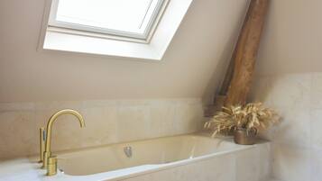 A bathroom with a freestanding bathtub, a skylight, and a potted plant.