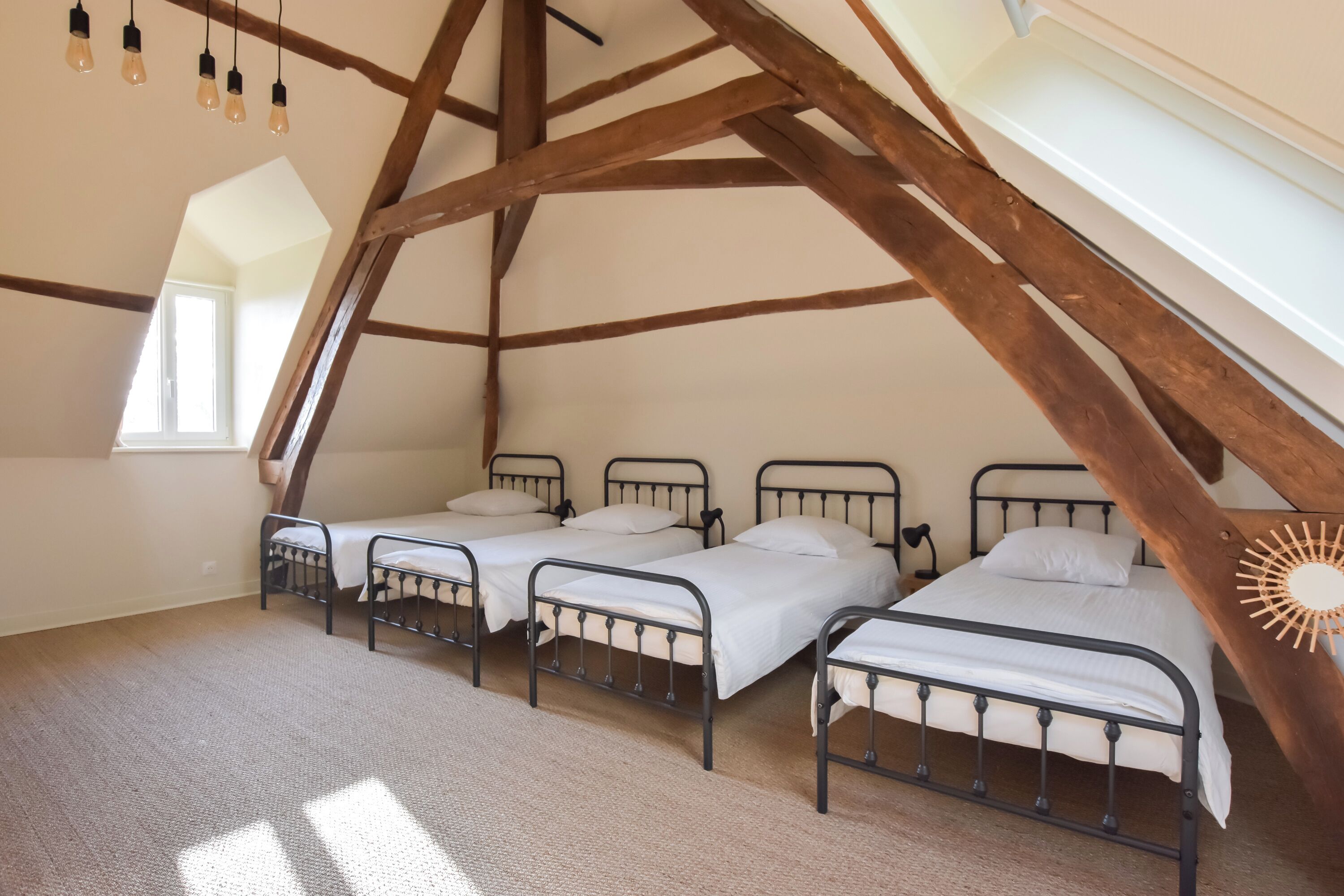 Ein Zimmer mit drei Metallbetten, einer geneigten Decke und einem Dachfenster.
