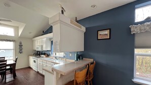 Una cocina con armarios blancos, una isla central y sillas de madera.