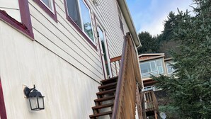 Una escalera de madera que conduce a una casa con fachada blanca y detalles en rojo.