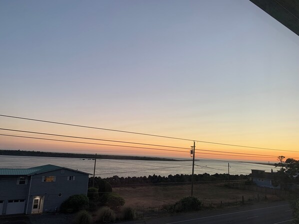 Vista costera con carretera, una casa pequeña y una masa de agua durante la puesta de sol.