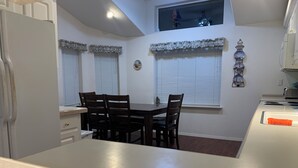 Una cocina compacta con una mesa y sillas, un refrigerador y una ventana con una cortina decorativa.