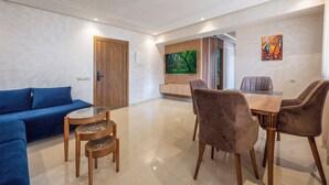 Un salon moderne avec un canapé bleu, une table basse en bois et un coin repas comprenant une table en marbre et des chaises en velours.