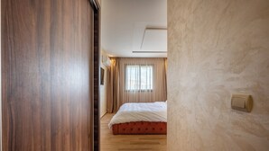 Une chambre avec un plancher en bois, un lit recouvert d’une couette blanche et une fenêtre avec des rideaux.