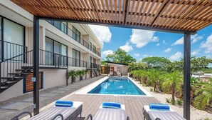 Zona de piscina con sillones de descanso y una pérgola de madera.