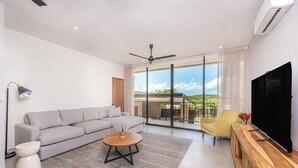 Una sala de estar moderna con un sofá gris, una mesa de centro redonda, un sillón amarillo y un televisor sobre un mueble de madera.