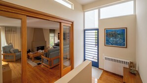 Ein geräumiges Wohnzimmer mit Holzboden, einer Couch, einem Couchtisch und einem Kamin. Es gibt ein großes Fenster mit Jalousien und ein Bild an der Wand.