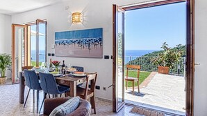 A dining area with a table set for four, a painting of a beach scene, and a view of the sea through large glass doors.