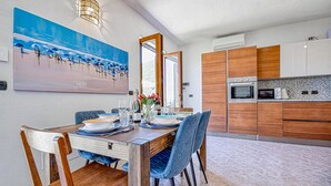A modern dining area with a wooden table set for four, a large painting above the table, and a kitchen with wooden cabinets and appliances.