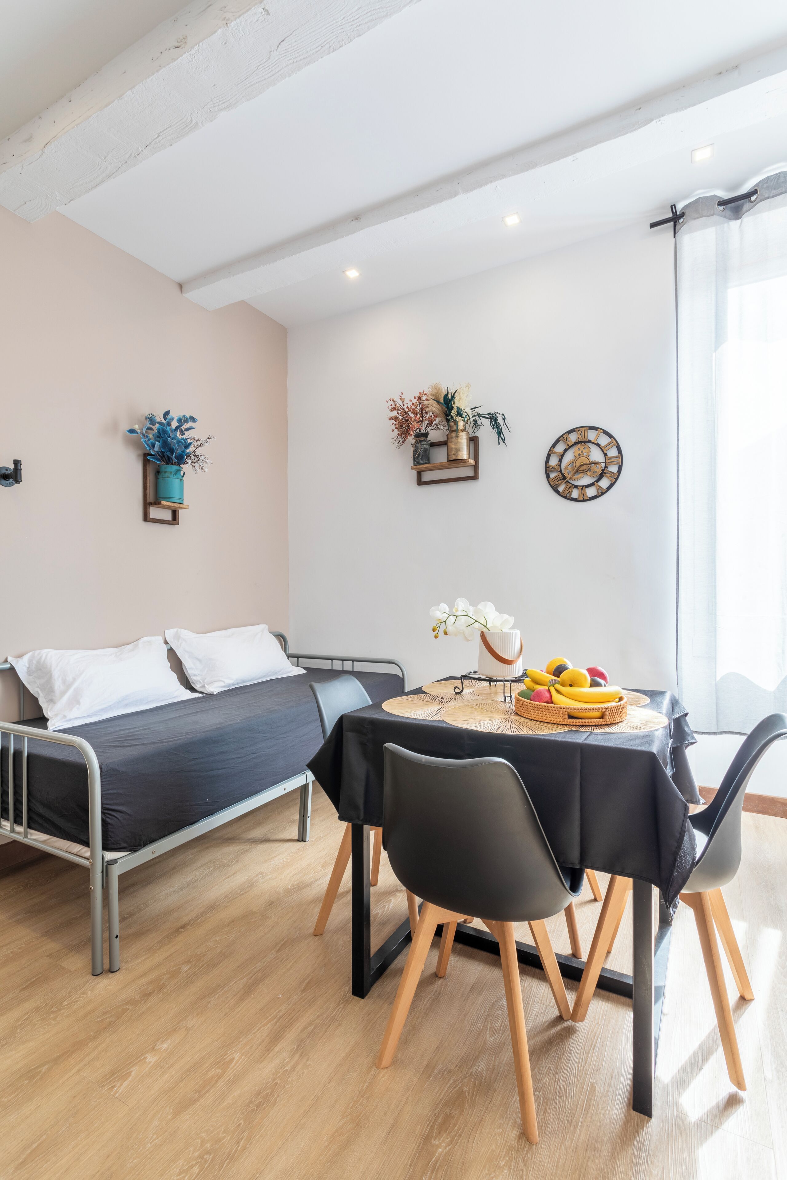 Una habitación moderna con una cama, una mesa de comedor con sillas, un reloj y objetos decorativos en la pared.