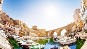 Una marina con barcos amarrados, un puente de piedra y edificios a lo largo del paseo marítimo.
