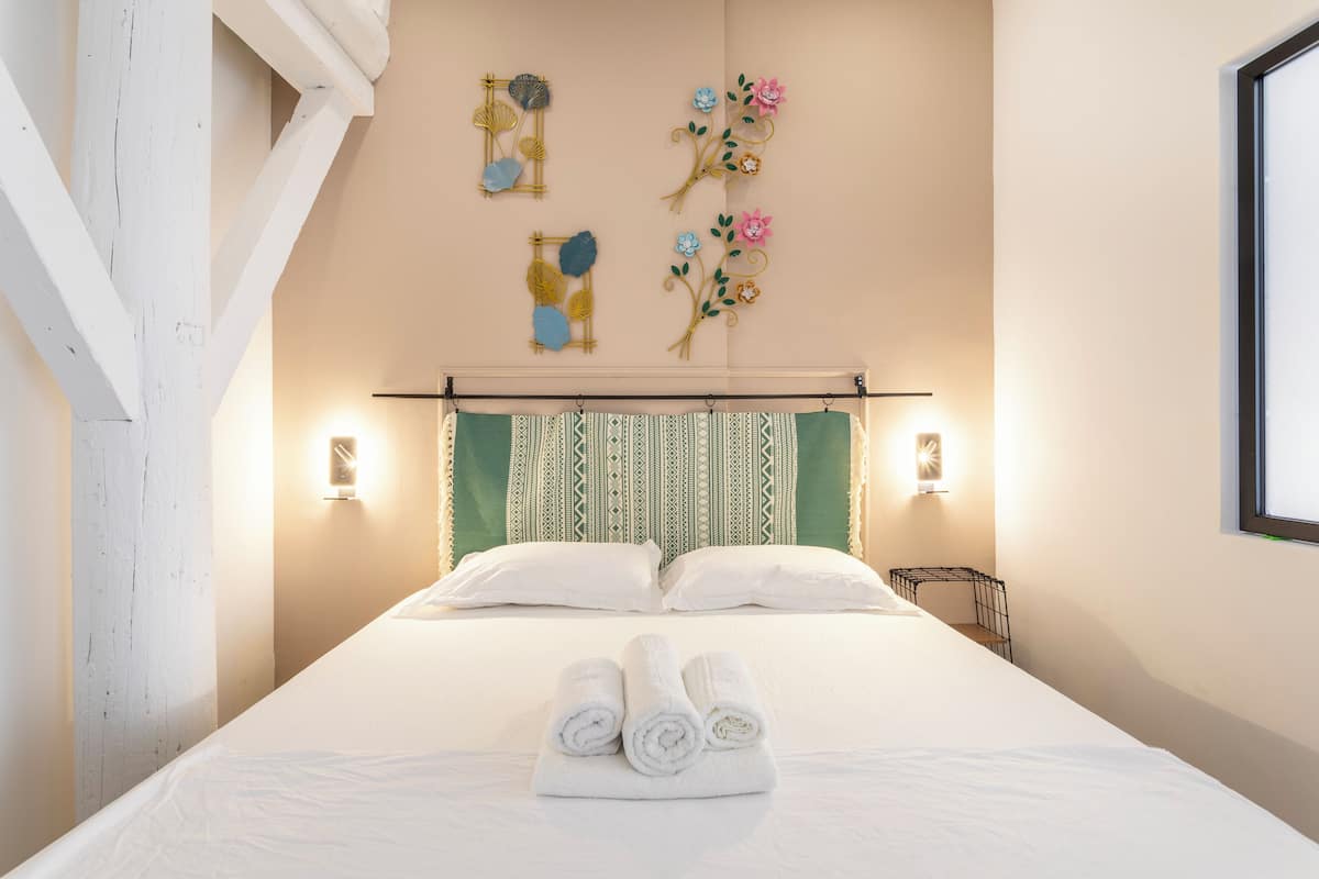 Un lit bien fait, avec des serviettes pliées, une tête de lit à motifs verts et blancs, et des objets décoratifs fixés au mur.