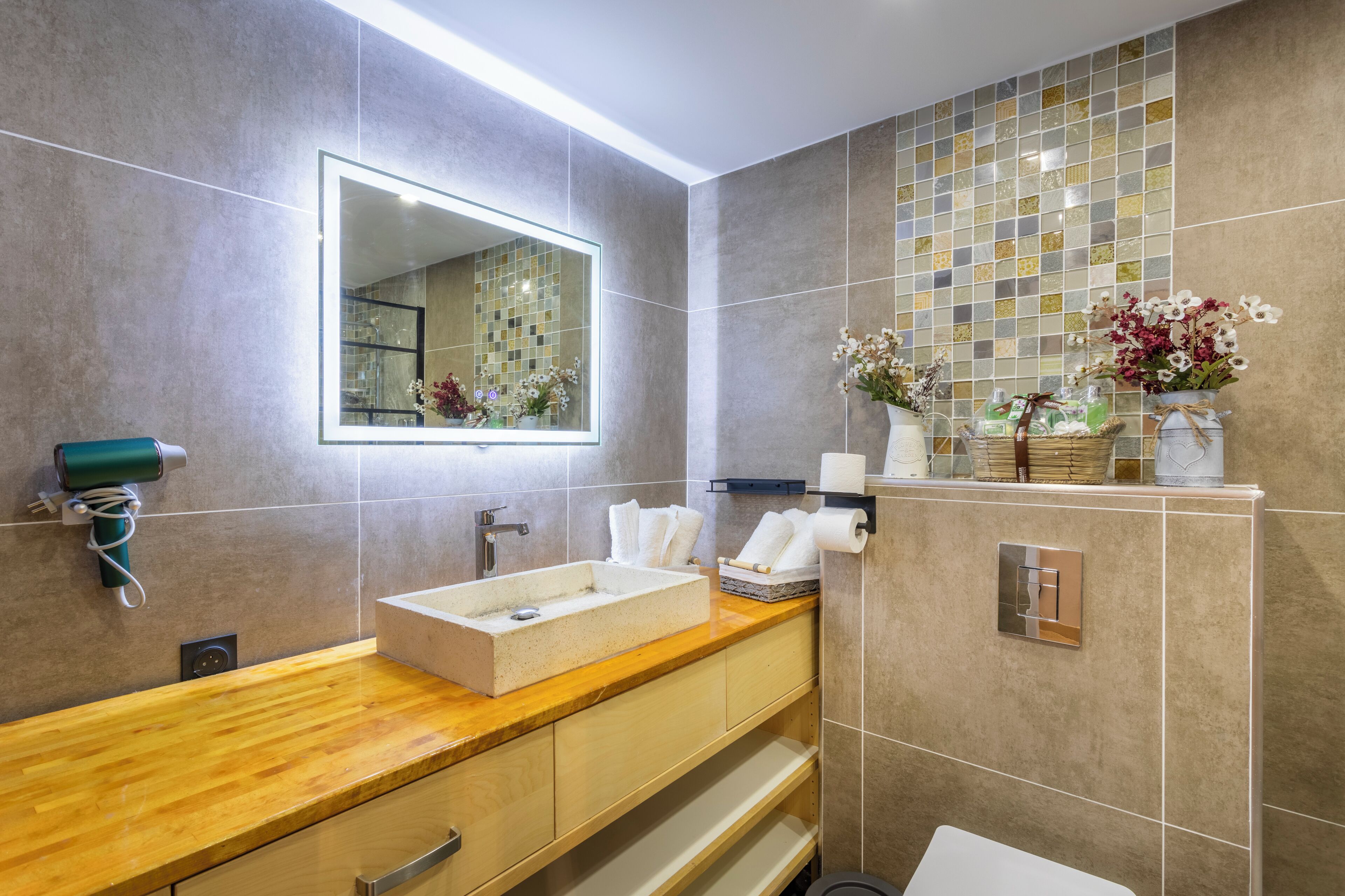 Un baño moderno con tocador de madera, un espejo grande y un salpicadero de azulejos.