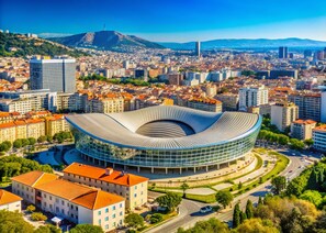 A modern stadium with a unique curved roof, surrounded by a cityscape with various buildings and a prominent hill in the background. - Adira Marseille Panier (Marseille)