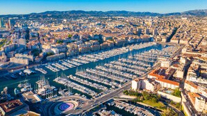 Marina con numerosas embarcaciones amarradas, rodeada de edificios urbanos y un cielo despejado.
