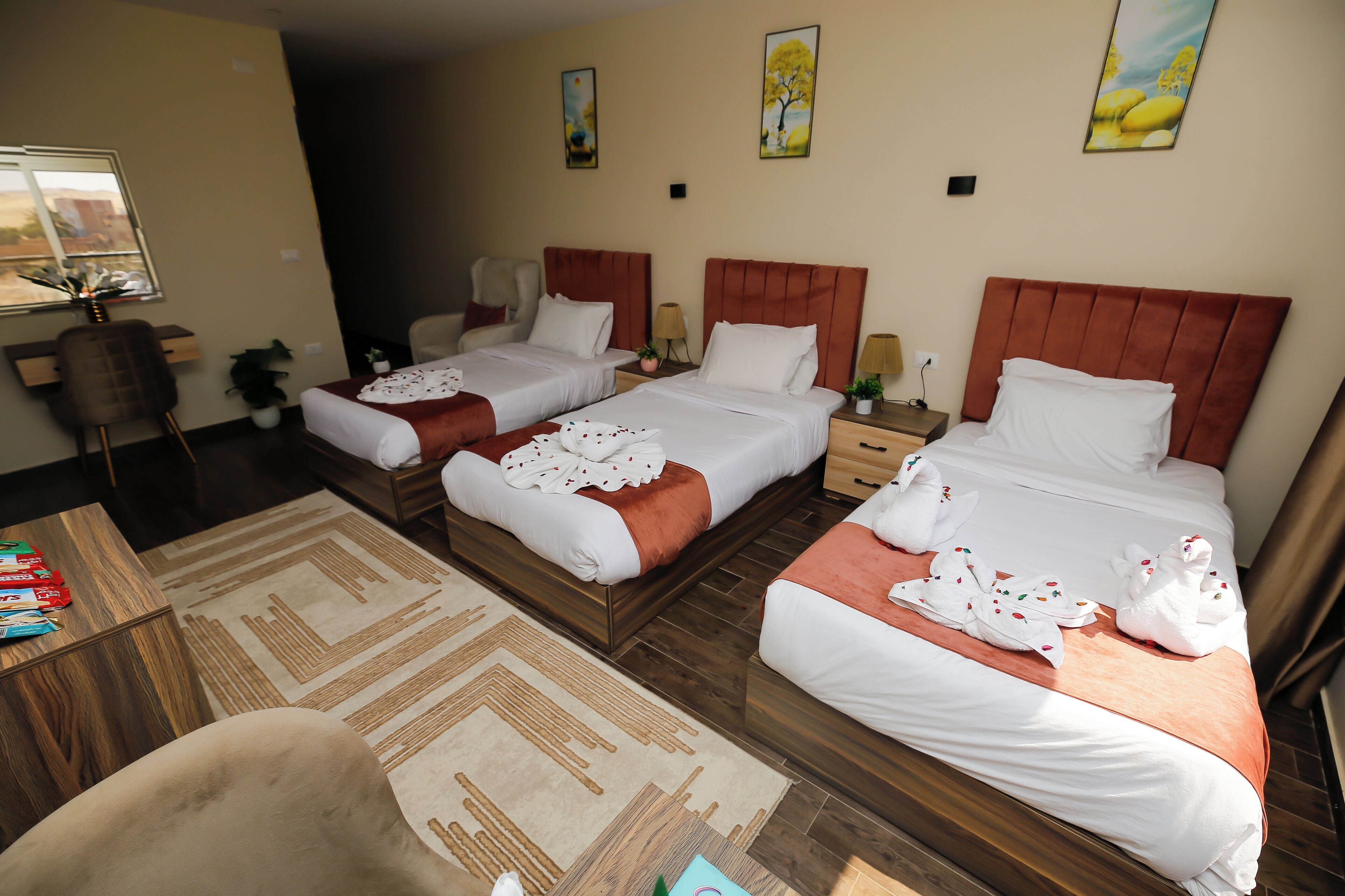 Habitación de hotel con dos camas, un escritorio y una silla. Hay dos mesitas de noche con lámparas, una ventana con vistas y un cuadro en la pared.
