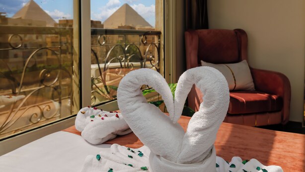 Une chambre d’hôtel avec vue sur les pyramides, une chaise rouge et une œuvre d’art réalisée avec des serviettes.