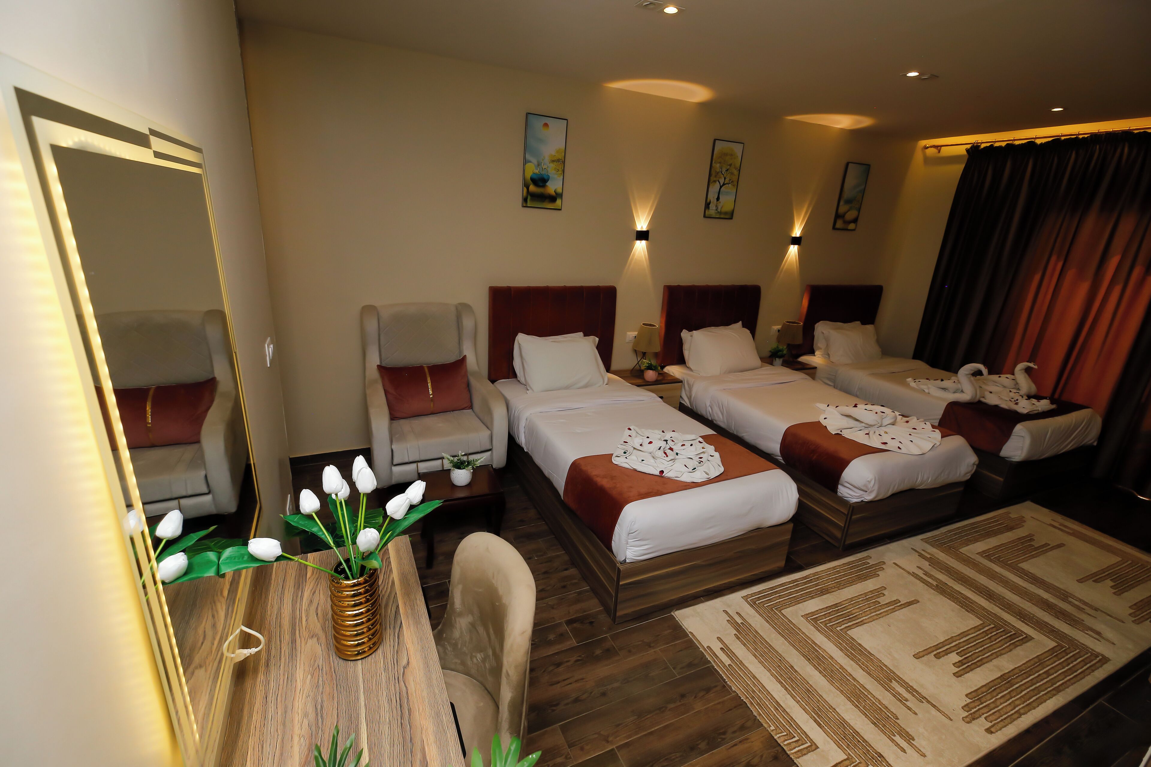 Een hotelkamer met twee enkele bedden, een slaapbank, een eettafel met een vaas bloemen en een grote spiegel.