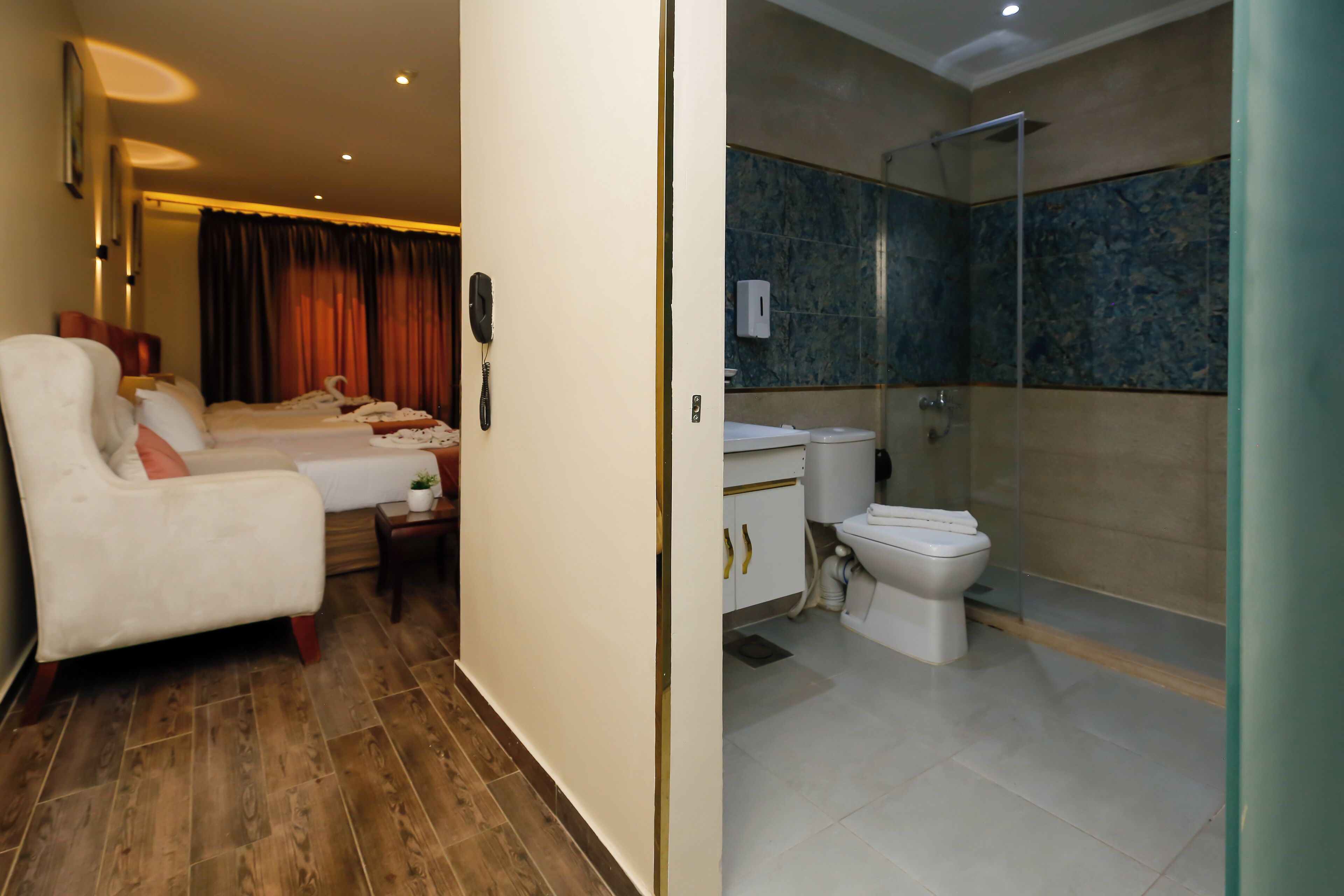 Una habitación de hotel con cama, una silla, mesita de noche, teléfono y baño con inodoro, lavabo y ducha.