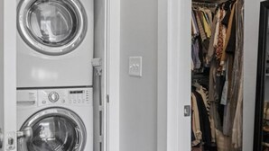 A laundry room with two stacked front-loading washing machines and a walk-in closet with hanging clothes. - Cozy townhome in charming Chattanooga downtown with fastest WiFi, sleep for 5  (Chattanooga)