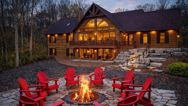 Un chalet doté d’un foyer en pierre et de chaises Adirondack rouges.