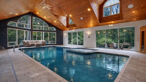 Une piscine intérieure dotée d’un plafond en bois, de grandes fenêtres et d’un espace détente.