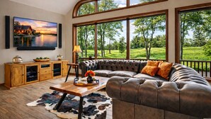 Un salon avec un canapé en cuir, une table basse en bois et une grande fenêtre donnant sur un paysage verdoyant.
