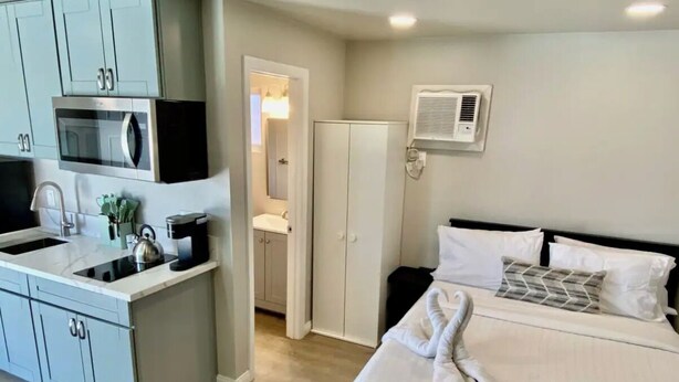A modern hotel room with a kitchenette, a bed with white linens, and a bathroom with a shower and toilet. - Cozy apartment with WiFi and AC in charming El Cajon San Diego (El Cajon)