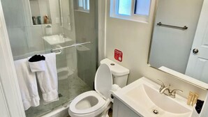 A modern bathroom with a glass-enclosed shower, a white toilet, and a sink with a mirror above it. - Cozy apartment with WiFi and AC in charming El Cajon San Diego (El Cajon)