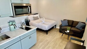 A compact living space with a kitchenette, a bed with a heart-shaped towel, a sofa, and a small table with a plant. - Cozy apartment with WiFi and AC in charming El Cajon San Diego (El Cajon)