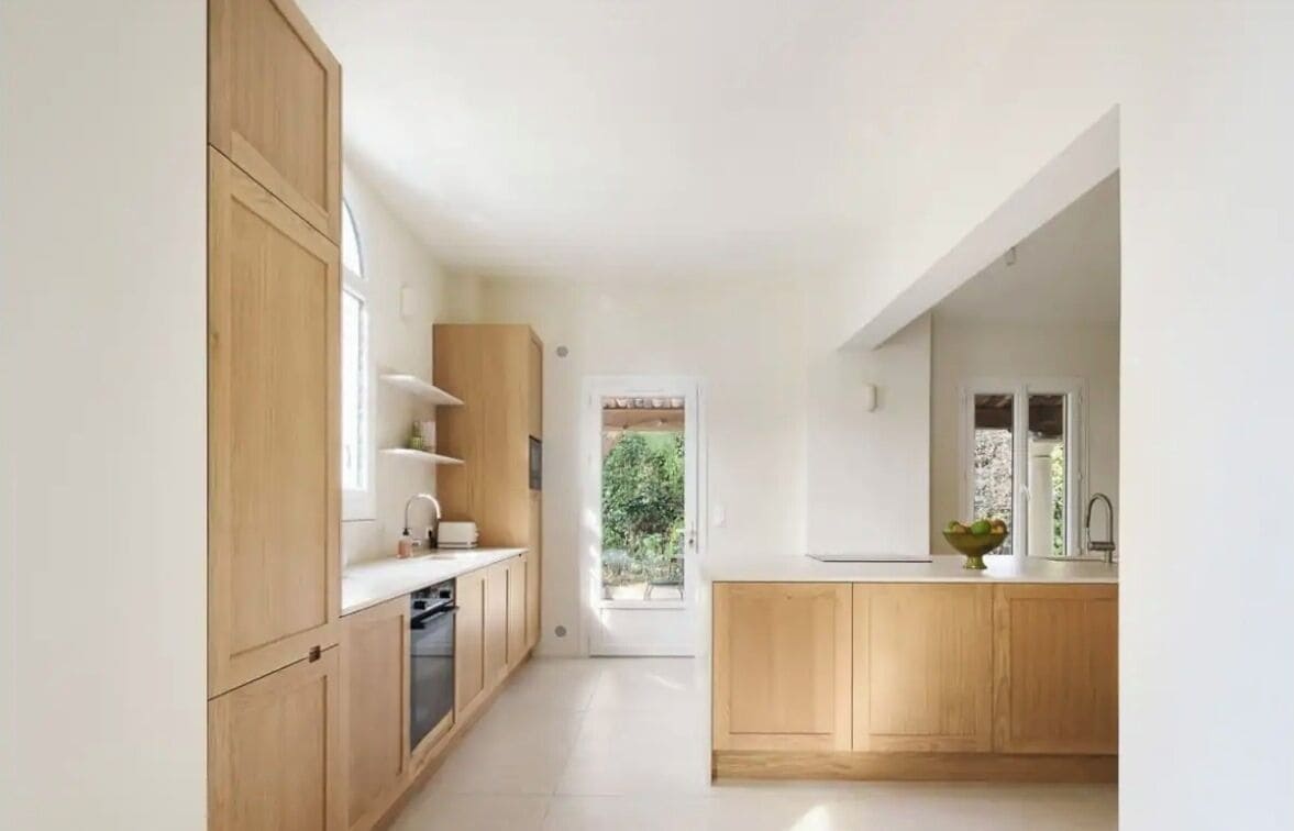 A modern kitchen with wooden cabinets, a central island, and a view to the outdoors.