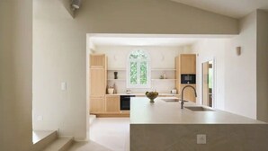 A modern kitchen with a central island, built-in appliances, and a large window. - Villa El Sol Juan Les Pins (Antibes)