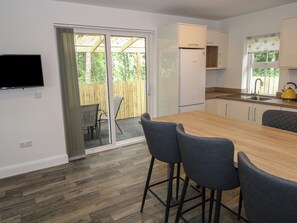 A modern kitchen with a wooden table, bar stools, a refrigerator, and a TV mounted on the wall. - CIARA'S PLACE, family friendly in Riverstown, County Sligo (Riverstown)