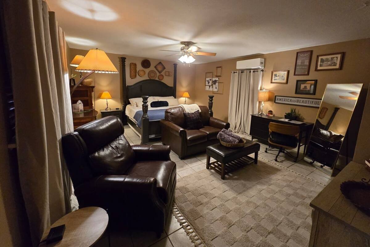 A cozy hotel room with a bed, leather armchair, sofa, and a desk with a chair.