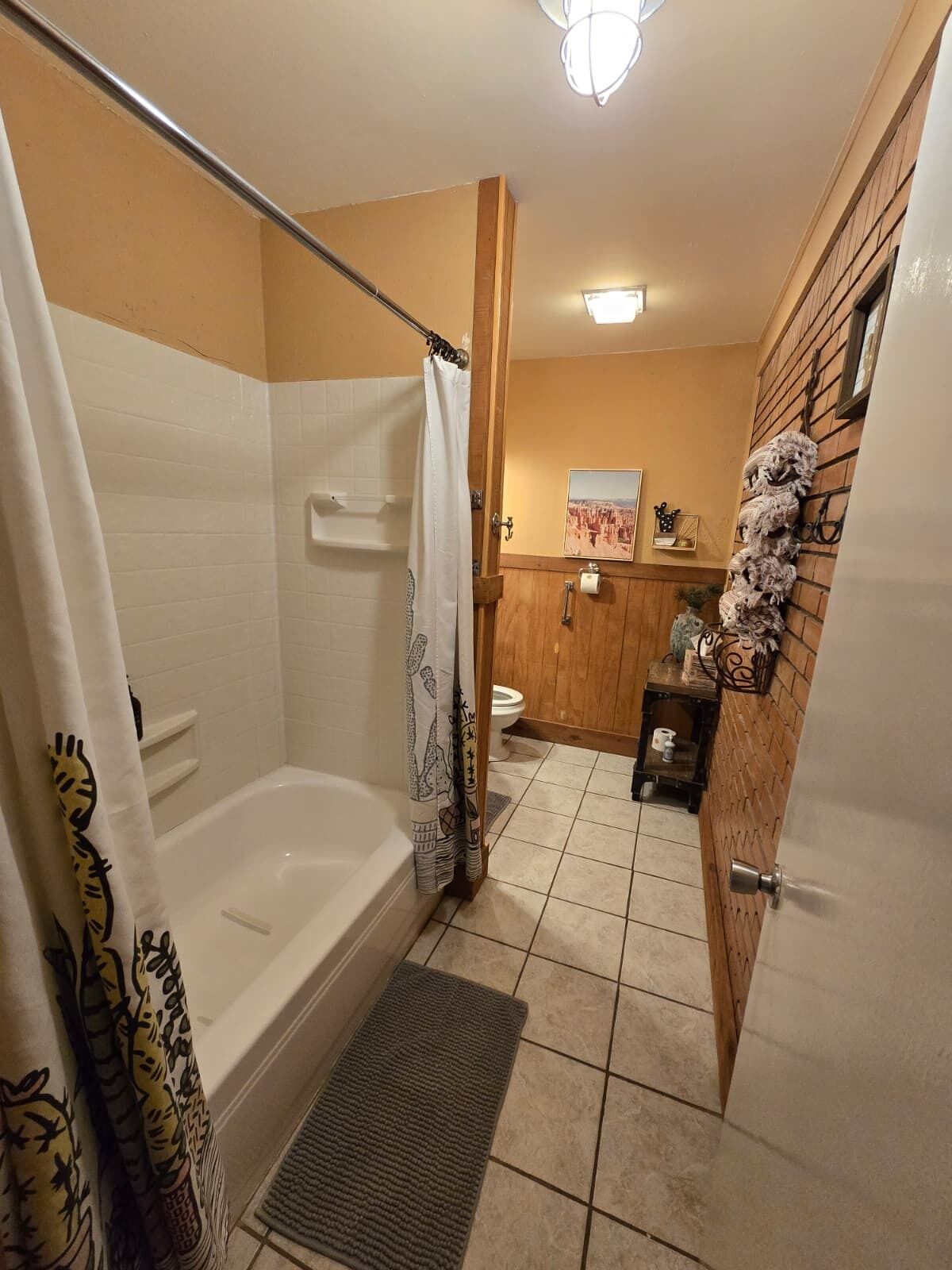 A bathroom with a bathtub, shower curtain, toilet, and a wooden wall with a decorative piece.