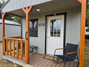 A wooden deck with a bench and a door, a small table, and a welcome mat. - Roots Retreat (Seymour)