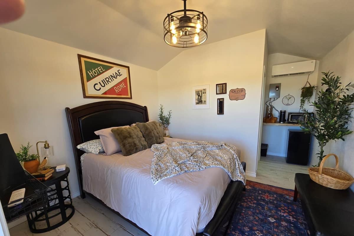 A hotel room with a bed, a desk, a chair, a lamp, and a decorative wall sign.