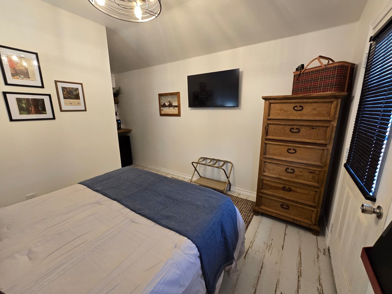 A bedroom with a bed, dresser, and wall-mounted TV.