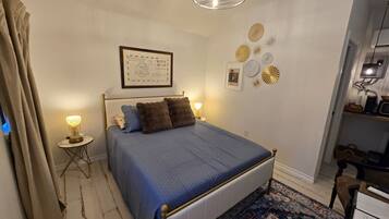 Un dormitorio con cama, una mesita de noche pequeña, una lámpara, un cuadro en la pared y una lámpara del techo.