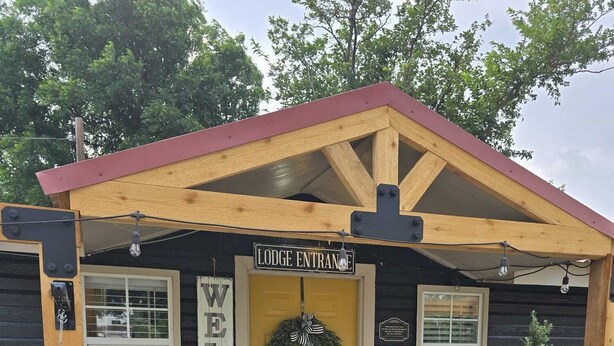 A lodge entrance with a yellow door, a welcome sign, and a wreath.