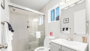 Une salle de bain moderne avec une douche à parois de verre, des toilettes blanches et un meuble-lavabo avec un miroir et un évier.