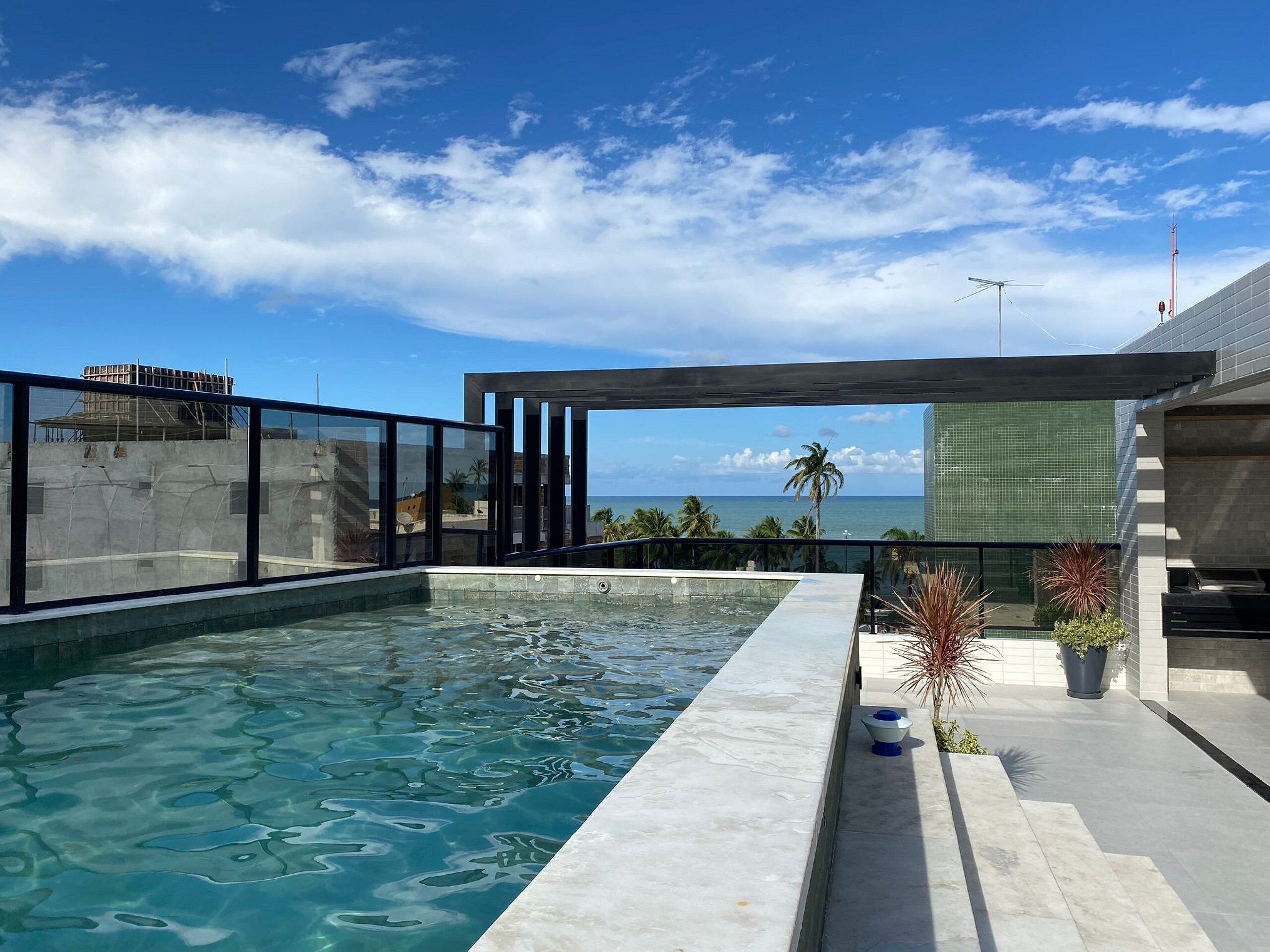 A rooftop infinity pool with clear blue water, a view of the ocean, and a modern architectural design.