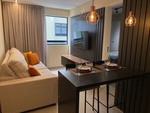 En moderne stue med sofa, spisebord og fjernsyn ophængt på væggen.